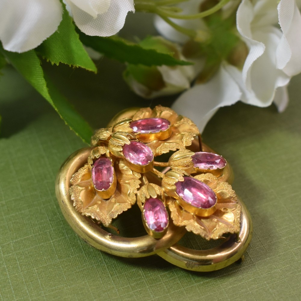 An early Victorian 15ct gold floral brooch featuring oval foil-backed pink topaz gemstones set amongst chased gold leaf and scroll motifs. View IV