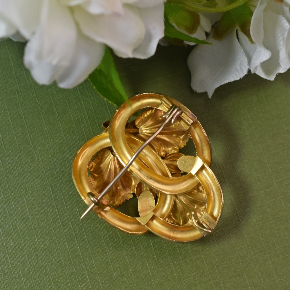 An early Victorian 15ct gold floral brooch featuring oval foil-backed pink topaz gemstones set amongst chased gold leaf and scroll motifs. View V