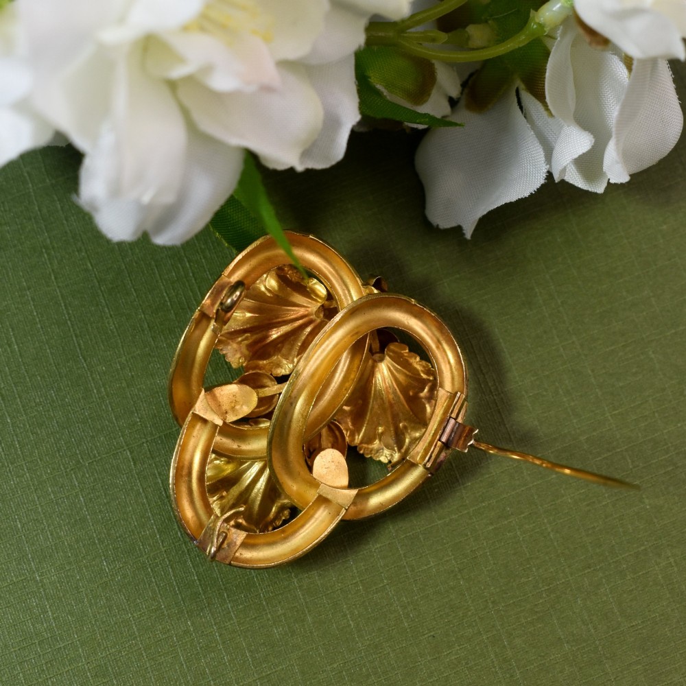 An early Victorian 15ct gold floral brooch featuring oval foil-backed pink topaz gemstones set amongst chased gold leaf and scroll motifs. View VI