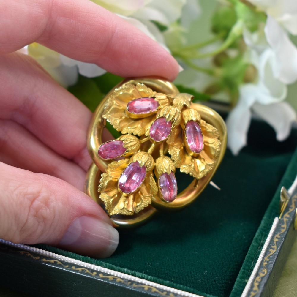 An early Victorian 15ct gold floral brooch featuring oval foil-backed pink topaz gemstones set amongst chased gold leaf and scroll motifs. View VII