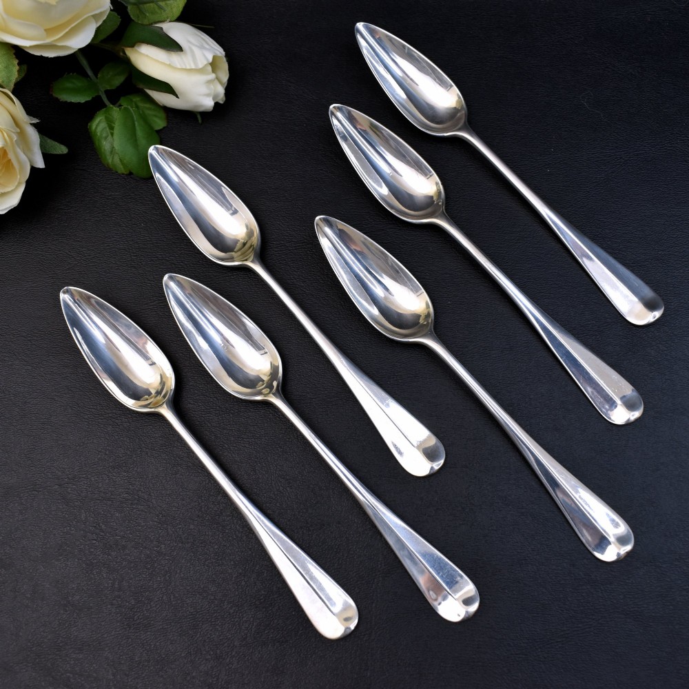 A set of six sterling silver grapefruit spoons with pointed bowls and tapered handles on a dark background.