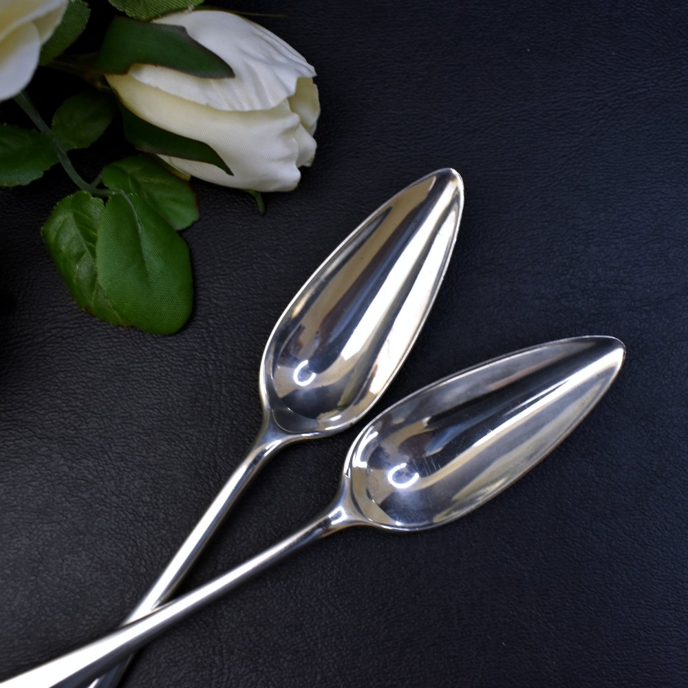 A set of six sterling silver grapefruit spoons with pointed bowls and tapered handles on a dark background. View IV
