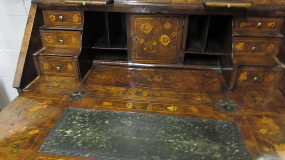 An 18th-century walnut bureau bookcase featuring intricate floral marquetry, a double-domed upper cabinet, a slant-front writing slope, and drawers raised on bun feet. View VI
