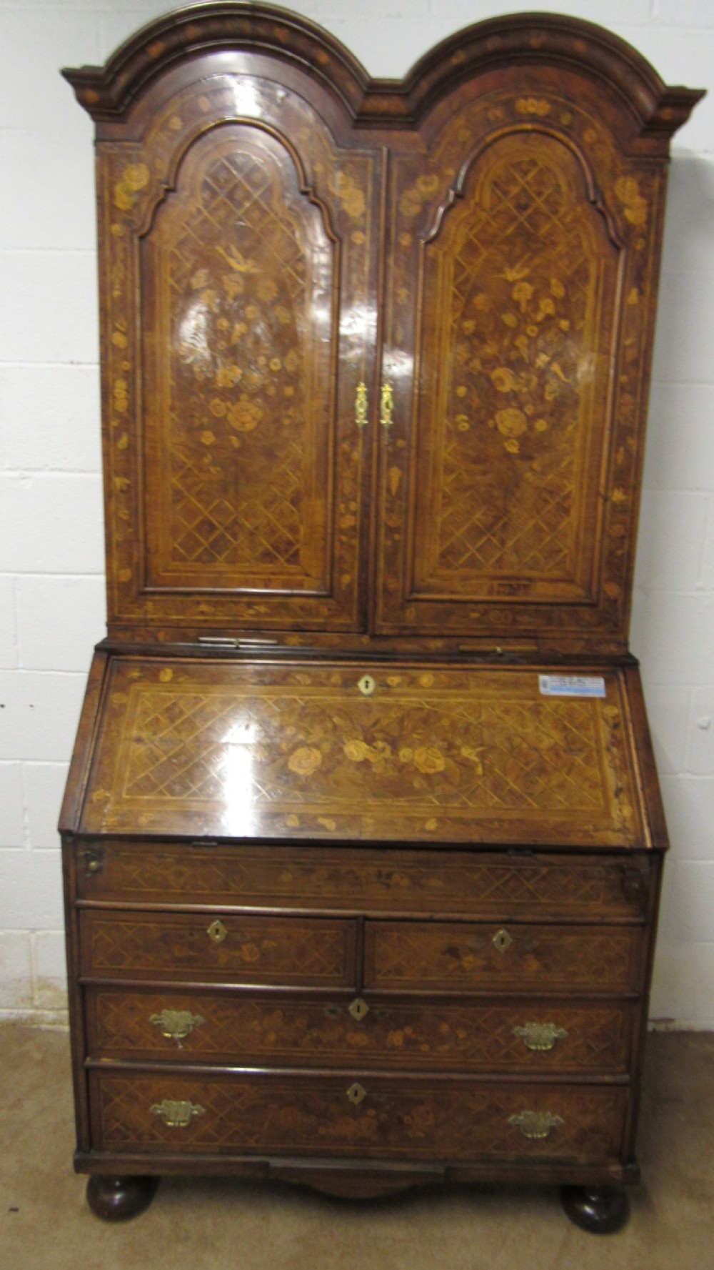 An 18th-century walnut bureau bookcase featuring intricate floral marquetry, a double-domed upper cabinet, a slant-front writing slope, and drawers raised on bun feet. View XII
