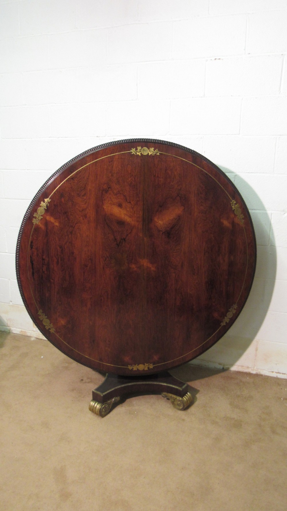 A circular Regency rosewood tilt-top loo table featuring brass marquetry inlay along the perimeter and a pedestal base.