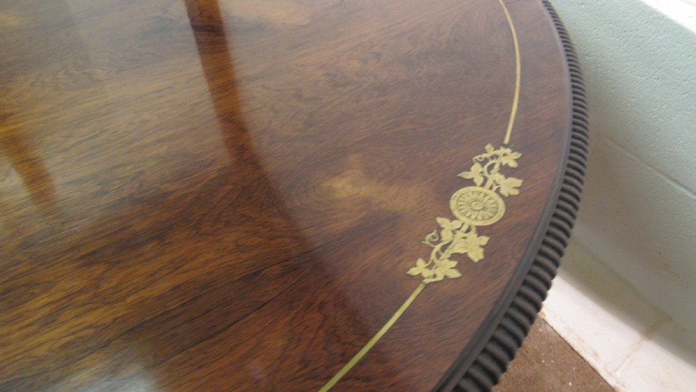 A circular Regency rosewood tilt-top loo table featuring brass marquetry inlay along the perimeter and a pedestal base. View VII
