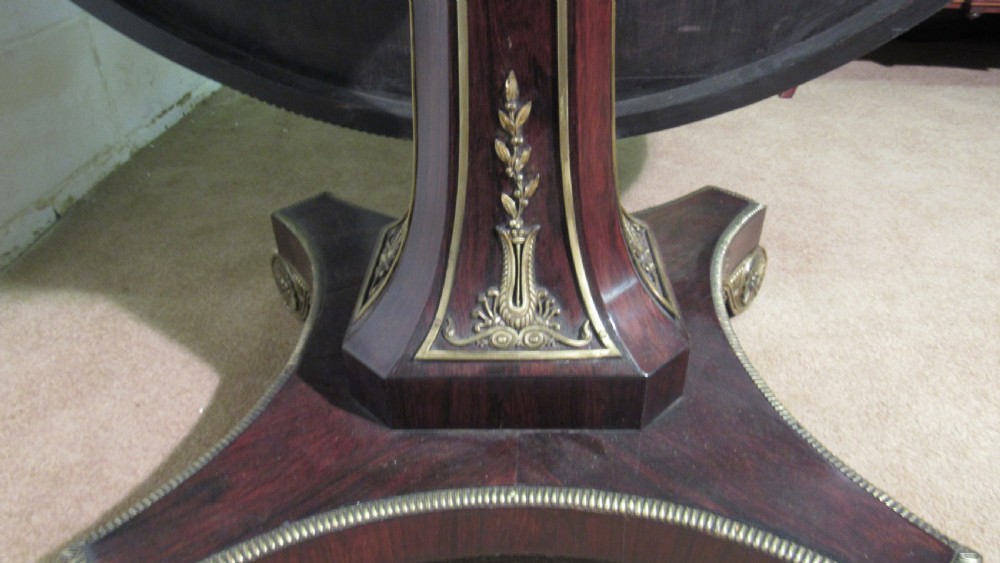 A circular Regency rosewood tilt-top loo table featuring brass marquetry inlay along the perimeter and a pedestal base. View X