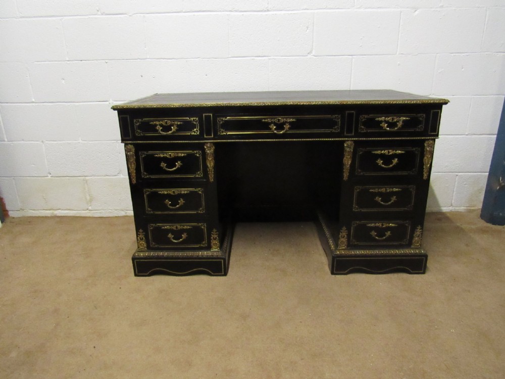 An ebonised black wood pedestal desk featuring decorative gilt-bronze ormolu mounts, multiple drawers, and brass handles.