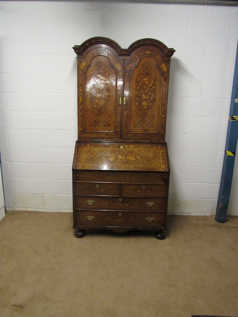 An 18th-century walnut bureau bookcase featuring intricate floral marquetry, a double-domed upper cabinet, a slant-front writing slope, and drawers raised on bun feet.