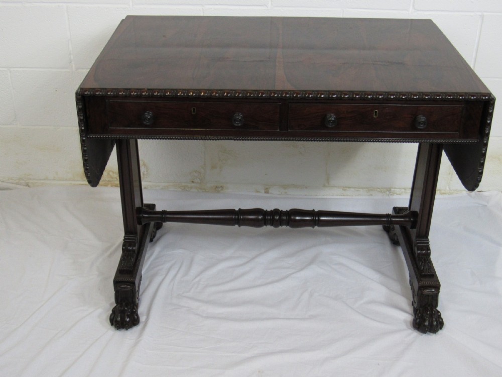 A 19th-century dark rosewood sofa table with two frieze drawers, drop-leaf side flaps, a turned central stretcher, and carved lion paw feet.