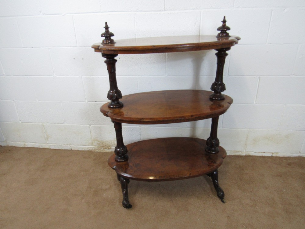 A Victorian burr walnut three-tier oval what-not etagere with turned columns, top finials, and carved feet on castors.