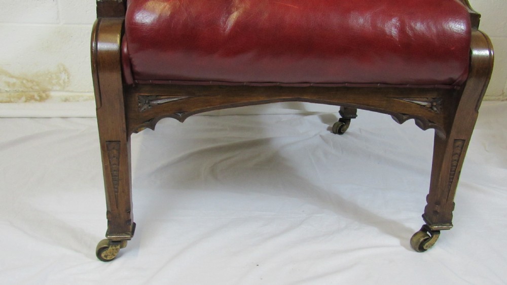A pair of high-backed Gothic Revival armchairs crafted from carved dark wood and upholstered in deep red leather with brass stud detail. View X