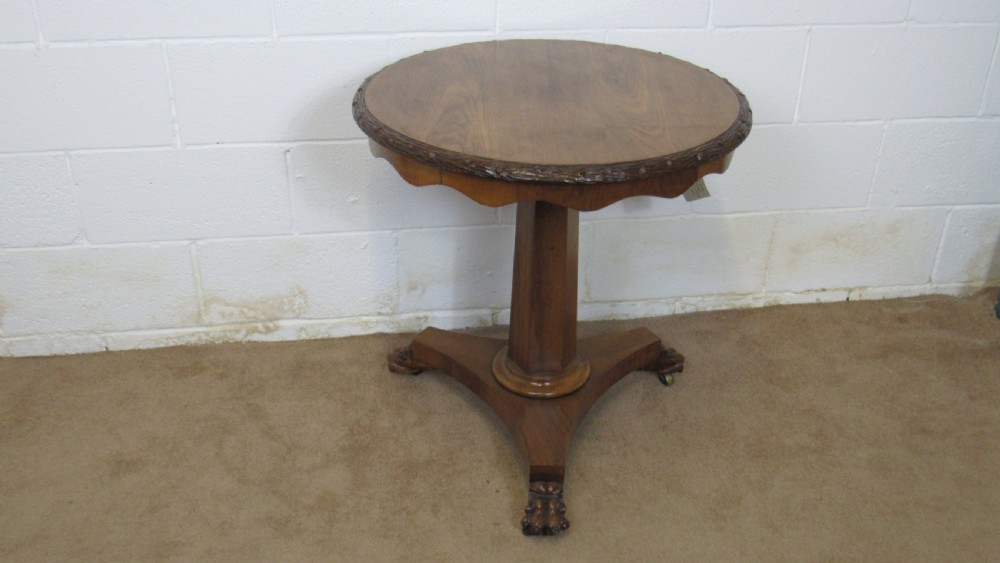 A circular 19th-century mahogany centre table with a carved rim, central pillar, and tri-form base with carved lion paw feet on brass castors.