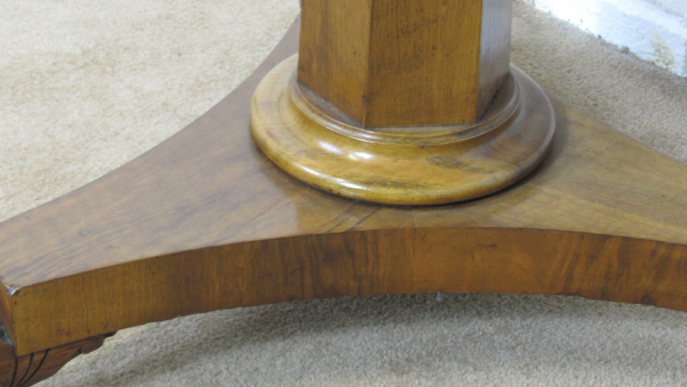 A circular 19th-century mahogany centre table with a carved rim, central pillar, and tri-form base with carved lion paw feet on brass castors. View VIII