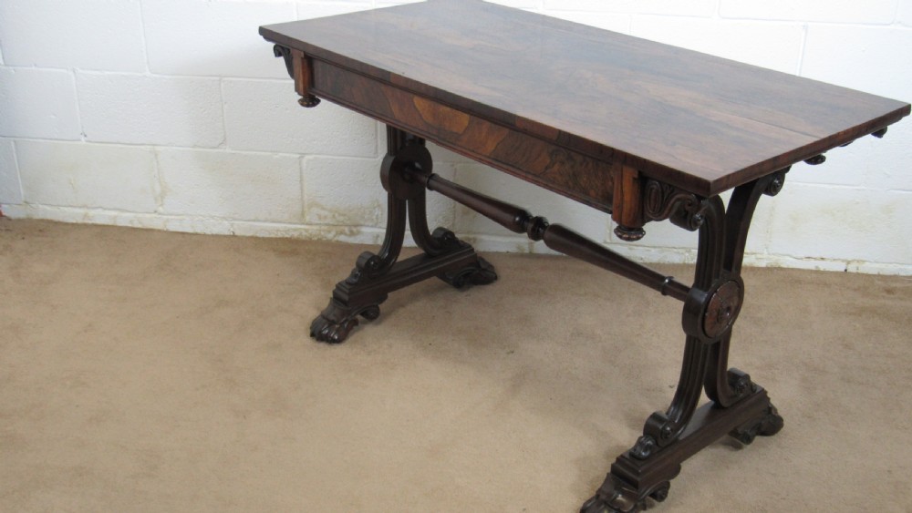 A dark rosewood library table featuring a polished rectangular top, frieze drawer, carved scroll trestle ends, a turned stretcher, and carved feet.