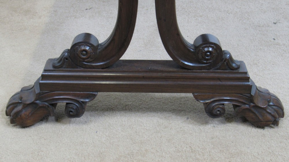 A dark rosewood library table featuring a polished rectangular top, frieze drawer, carved scroll trestle ends, a turned stretcher, and carved feet. View V