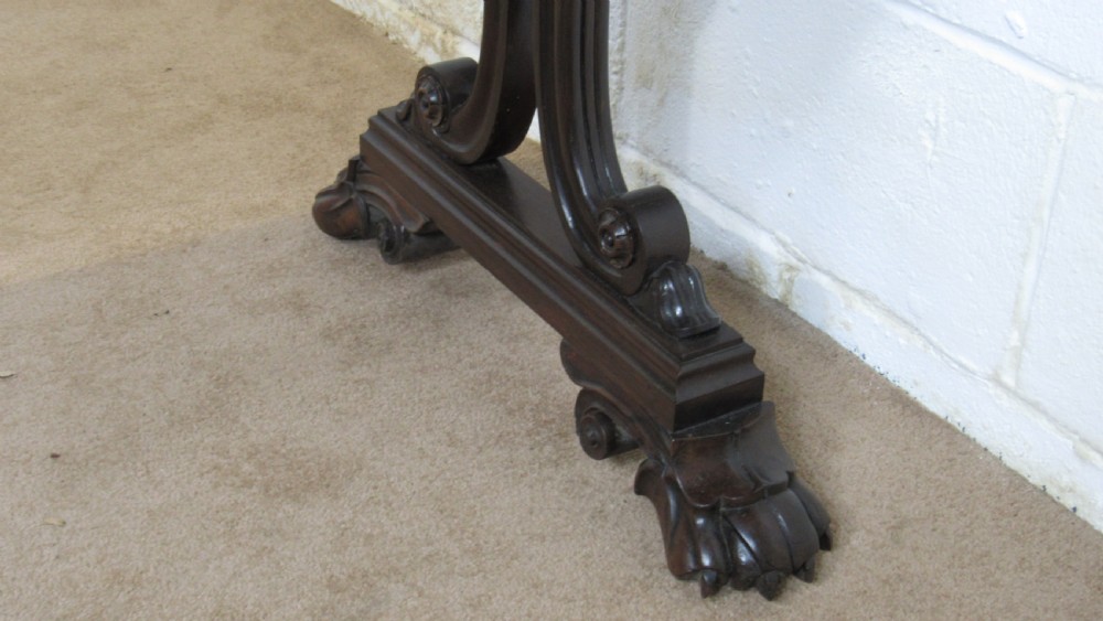 A dark rosewood library table featuring a polished rectangular top, frieze drawer, carved scroll trestle ends, a turned stretcher, and carved feet. View X