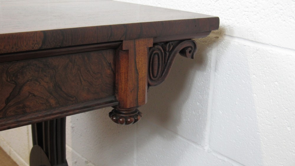 A dark rosewood library table featuring a polished rectangular top, frieze drawer, carved scroll trestle ends, a turned stretcher, and carved feet. View XI