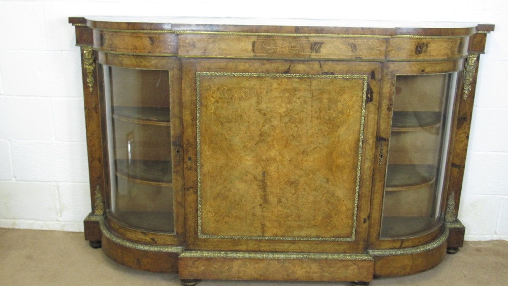 A Victorian burr walnut credenza featuring a central inlaid panel door flanked by two curved glazed display cupboards with gilt brass mounts.