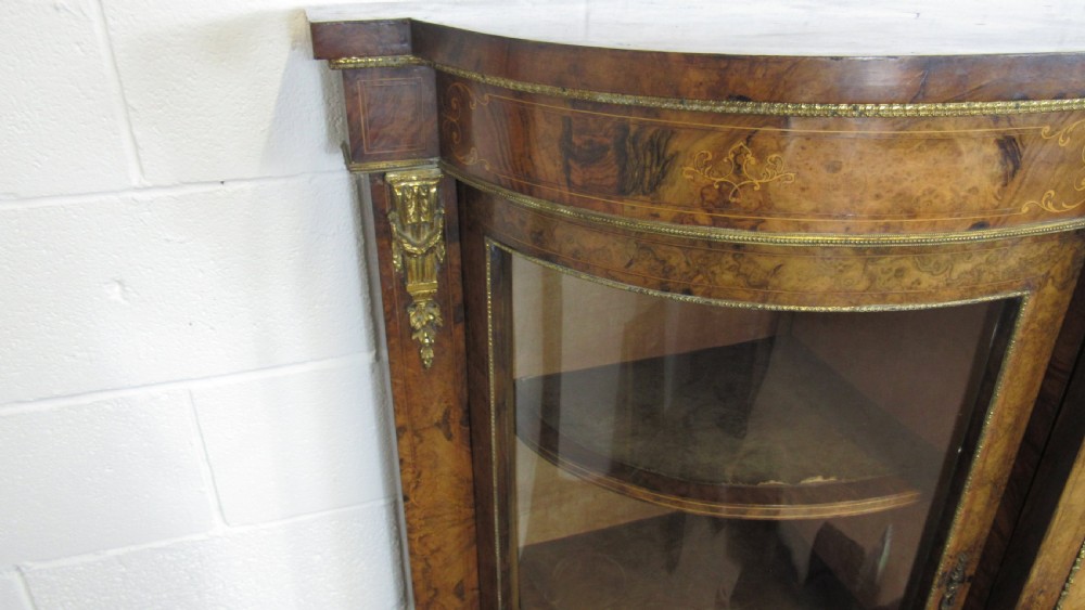 A Victorian burr walnut credenza featuring a central inlaid panel door flanked by two curved glazed display cupboards with gilt brass mounts. View XVI