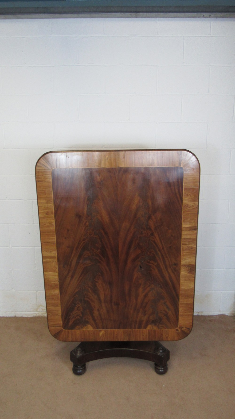 A 19th-century mahogany tilt-top centre table positioned vertically to show its flame-veneered surface and crossbanded border on a central pedestal base.
