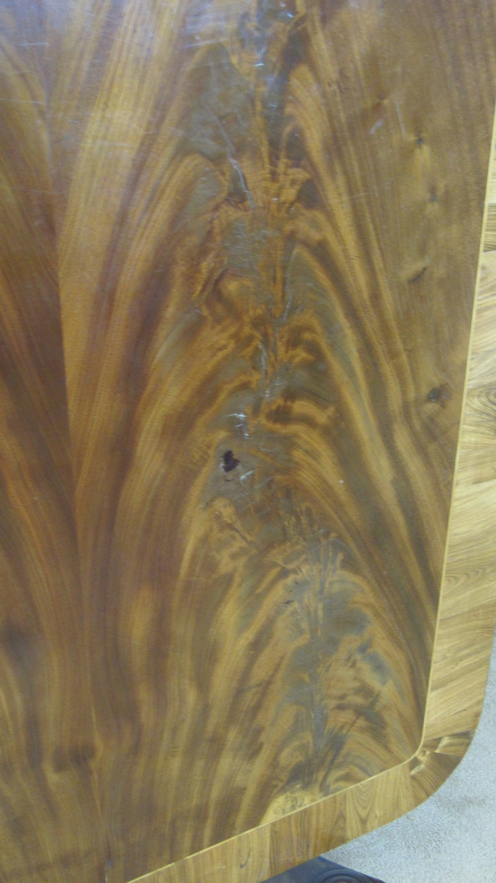 A 19th-century mahogany tilt-top centre table positioned vertically to show its flame-veneered surface and crossbanded border on a central pedestal base. View II