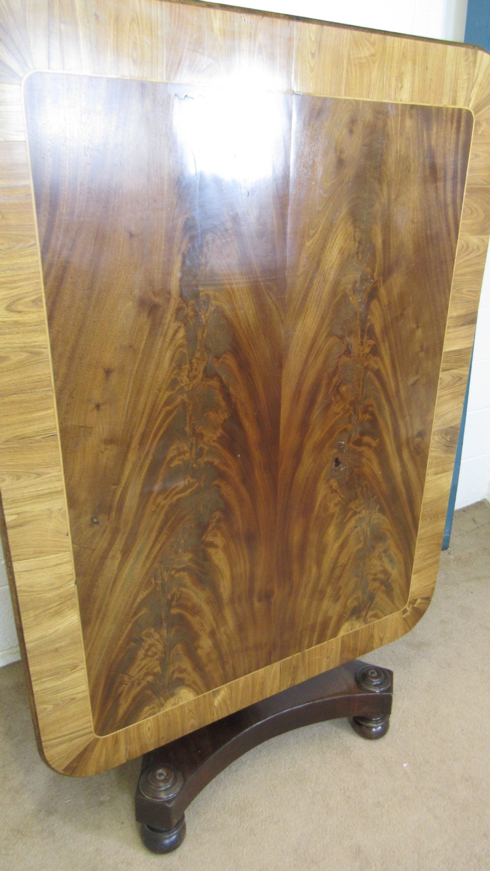 A 19th-century mahogany tilt-top centre table positioned vertically to show its flame-veneered surface and crossbanded border on a central pedestal base. View III