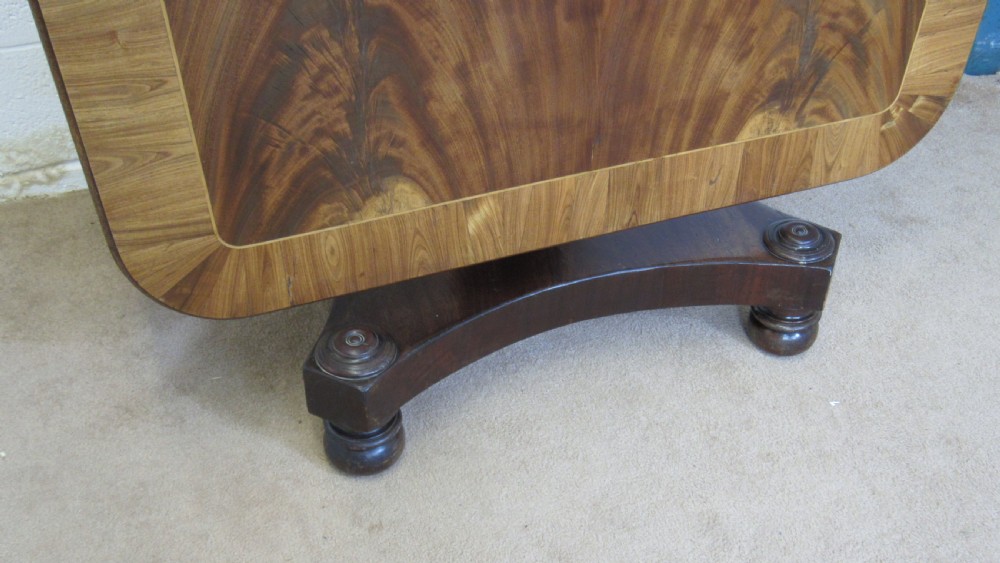 A 19th-century mahogany tilt-top centre table positioned vertically to show its flame-veneered surface and crossbanded border on a central pedestal base. View IV