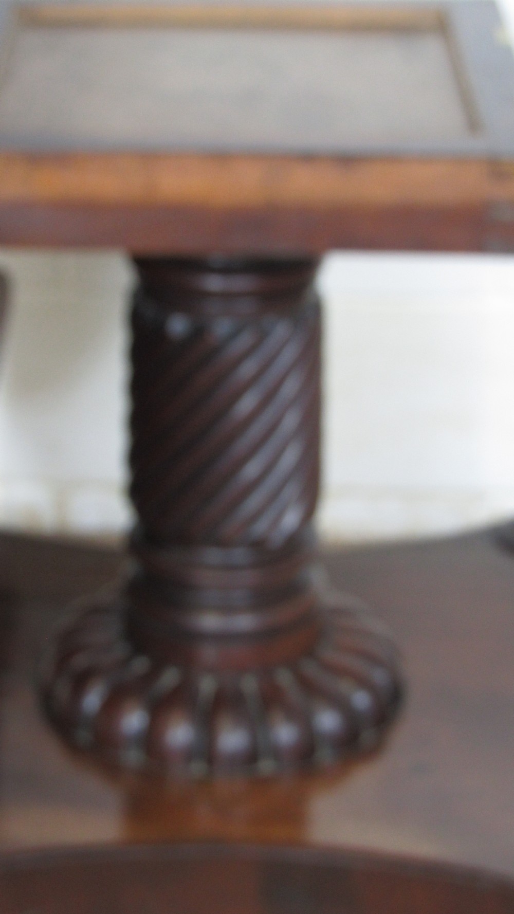 A 19th-century mahogany tilt-top centre table positioned vertically to show its flame-veneered surface and crossbanded border on a central pedestal base. View VI