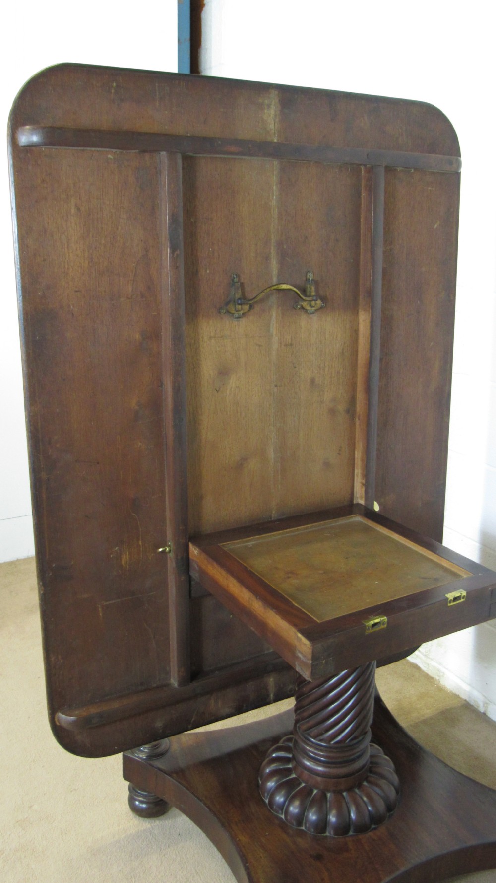 A 19th-century mahogany tilt-top centre table positioned vertically to show its flame-veneered surface and crossbanded border on a central pedestal base. View IX