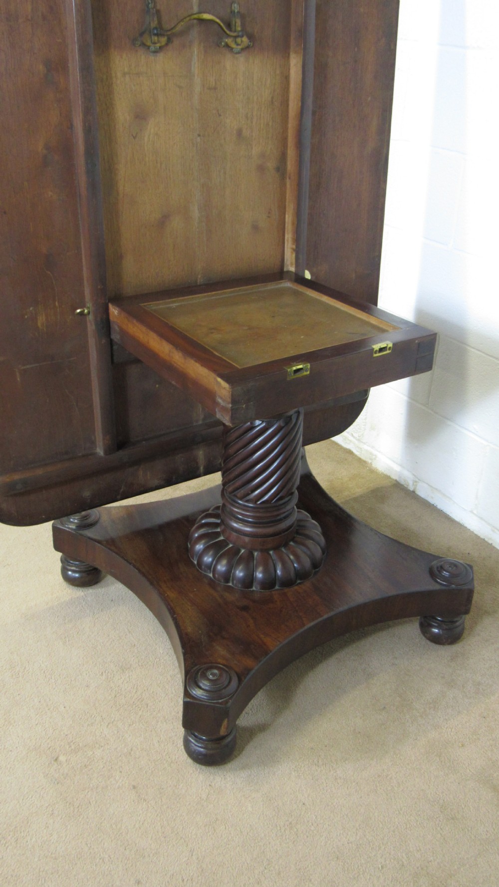A 19th-century mahogany tilt-top centre table positioned vertically to show its flame-veneered surface and crossbanded border on a central pedestal base. View X