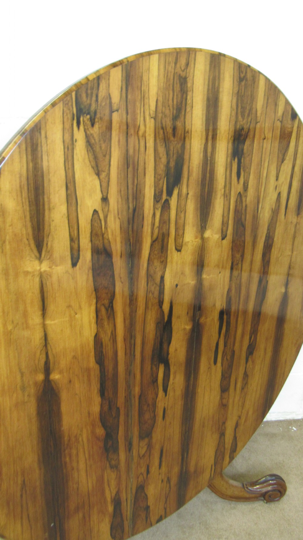 A circular antique rosewood tilt-top table shown in a vertical tilted position, displaying figured timber grain and a carved tripod base. View VI