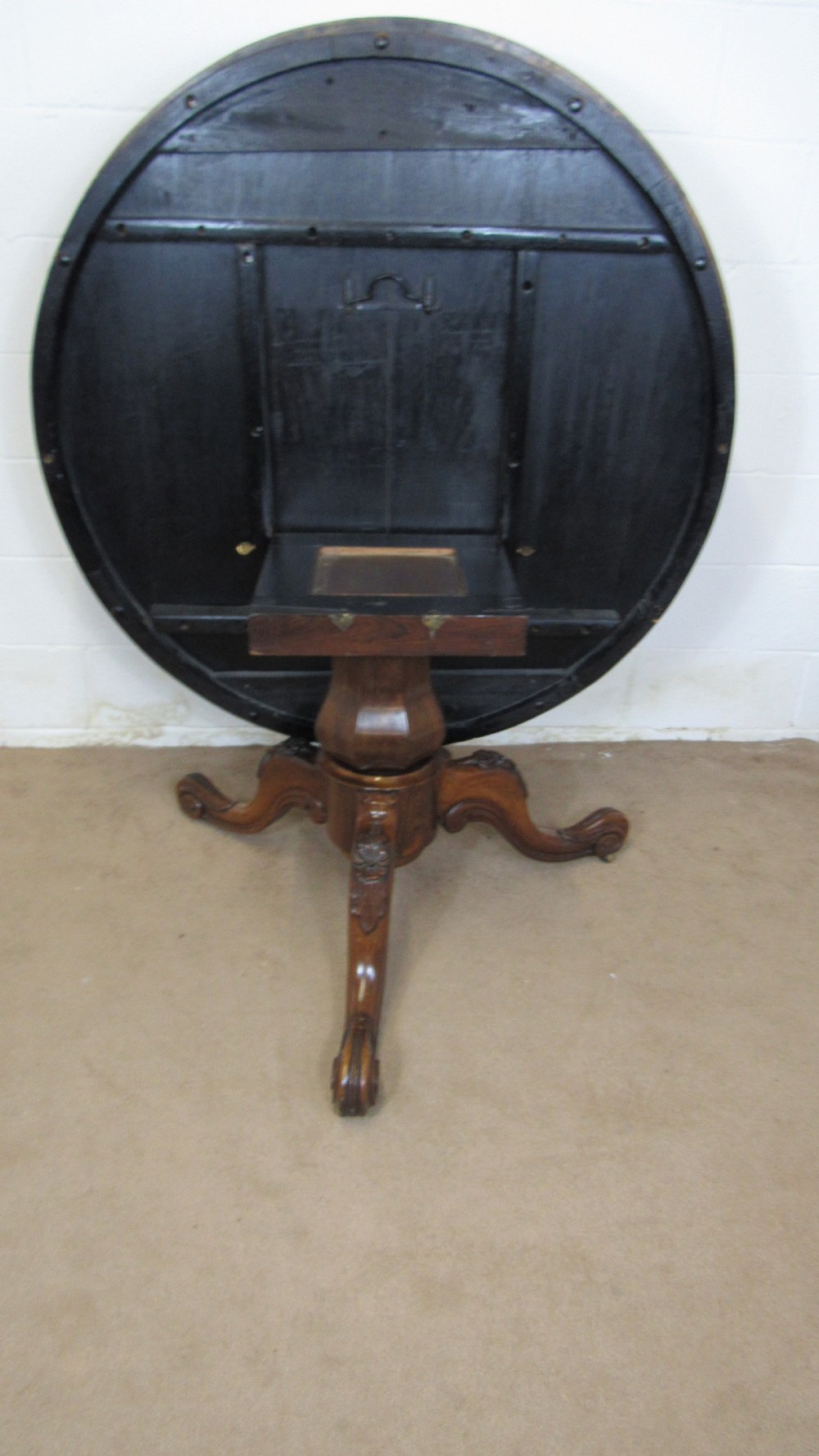 A circular antique rosewood tilt-top table shown in a vertical tilted position, displaying figured timber grain and a carved tripod base. View VII