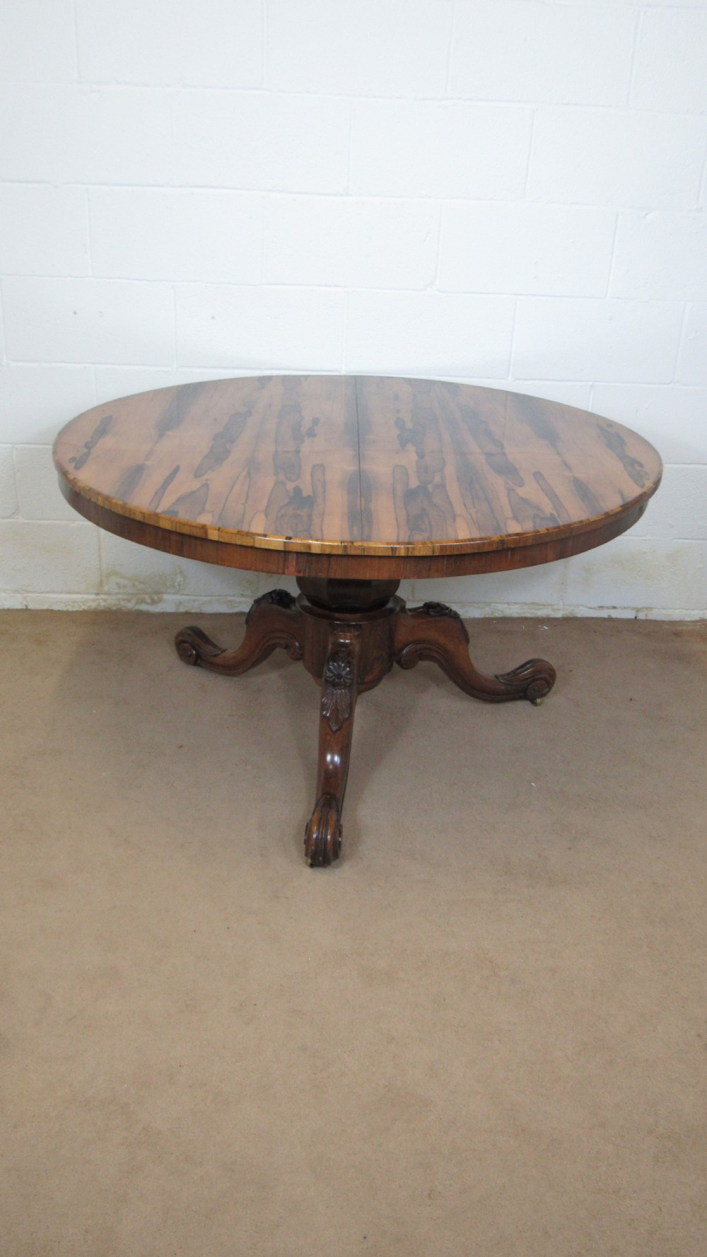 A circular antique rosewood tilt-top table shown in a vertical tilted position, displaying figured timber grain and a carved tripod base. View XIII