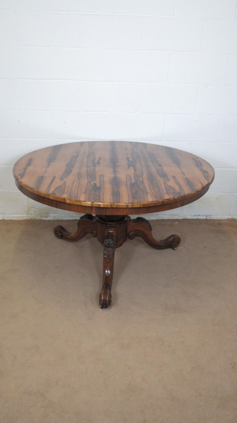 A circular antique rosewood tilt-top table shown in a vertical tilted position, displaying figured timber grain and a carved tripod base. View XIV