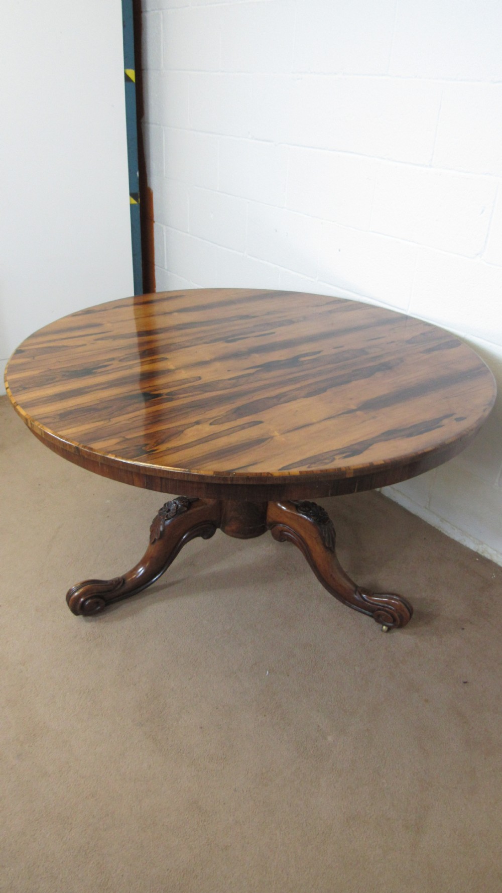 A circular antique rosewood tilt-top table shown in a vertical tilted position, displaying figured timber grain and a carved tripod base. View XV