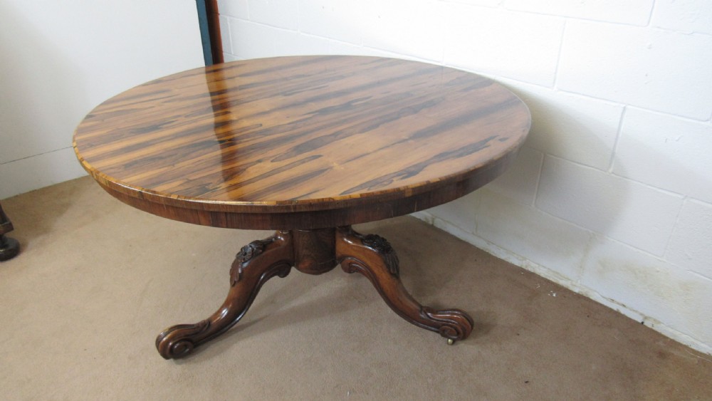 A circular antique rosewood tilt-top table shown in a vertical tilted position, displaying figured timber grain and a carved tripod base. View XVI