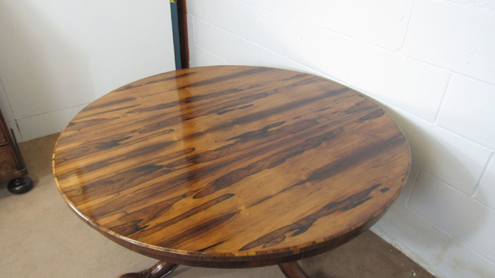 A circular antique rosewood tilt-top table shown in a vertical tilted position, displaying figured timber grain and a carved tripod base. View XVII
