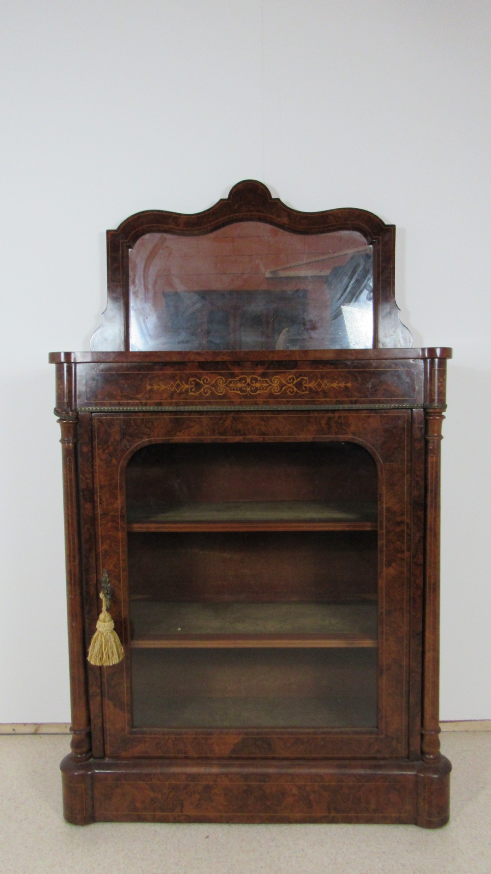 Victorian burr walnut pier cabinet featuring a glazed single door, scrollwork marquetry inlay, side columns, and an arched mirror back.