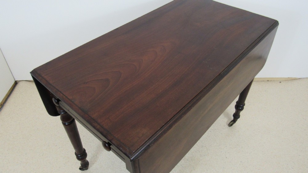 A dark mahogany Pembroke table with two drop leaves, turned legs on brass castors, and a single end drawer with wooden knobs. View II
