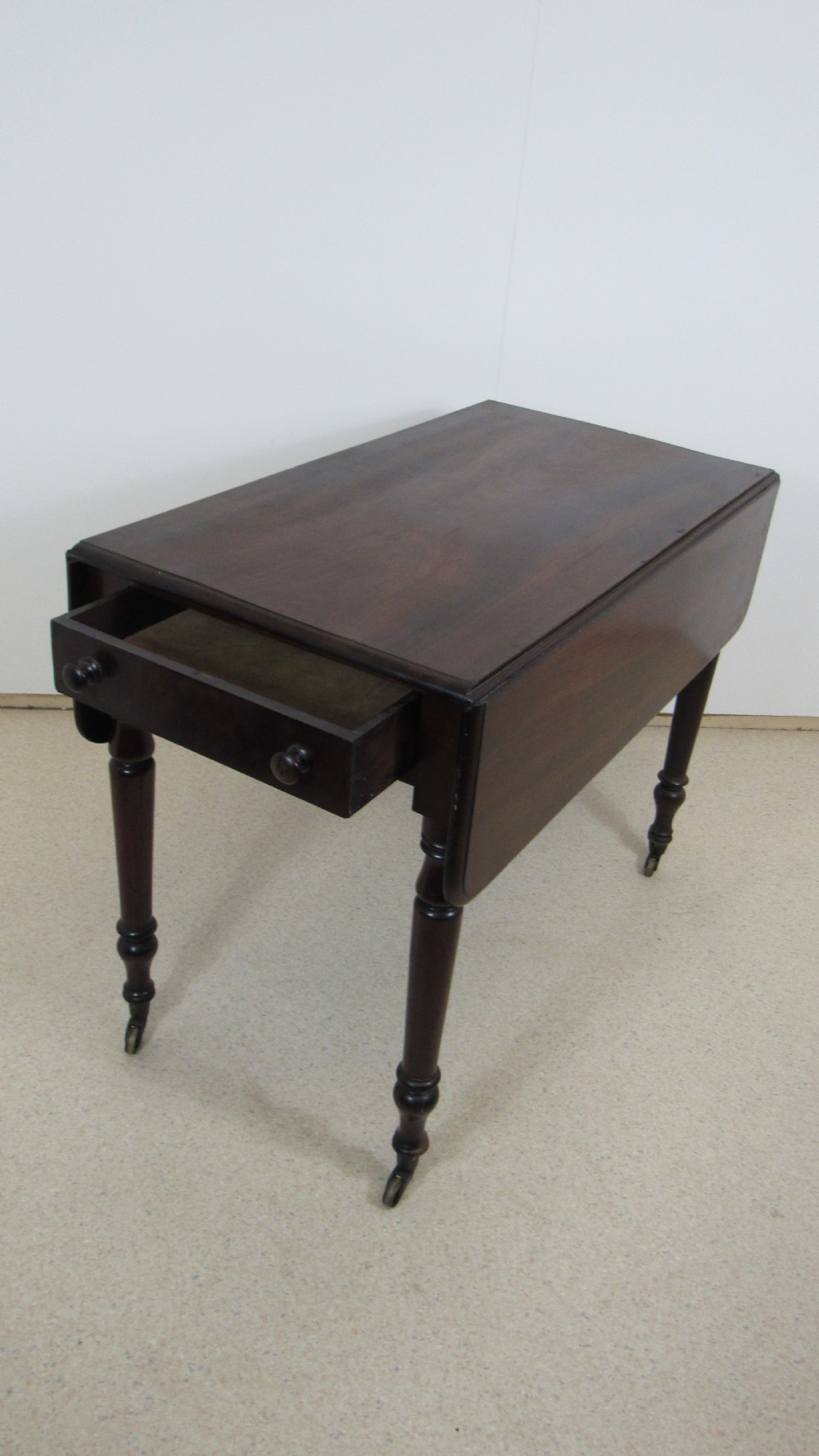 A dark mahogany Pembroke table with two drop leaves, turned legs on brass castors, and a single end drawer with wooden knobs. View III