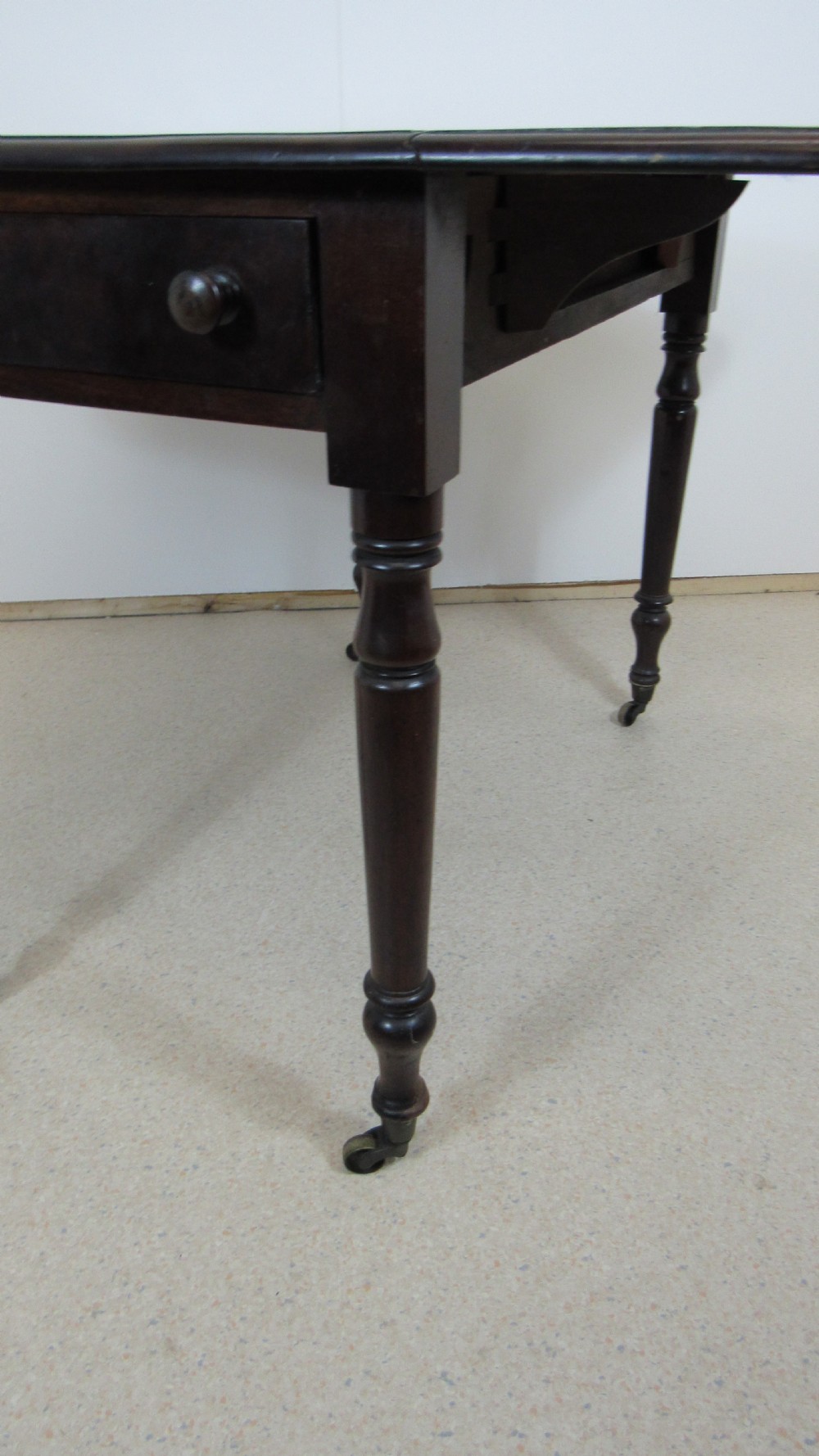 A dark mahogany Pembroke table with two drop leaves, turned legs on brass castors, and a single end drawer with wooden knobs. View IX