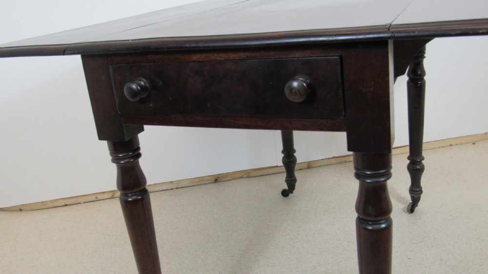 A dark mahogany Pembroke table with two drop leaves, turned legs on brass castors, and a single end drawer with wooden knobs. View XI