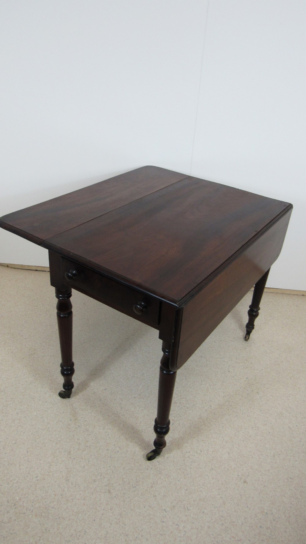 A dark mahogany Pembroke table with two drop leaves, turned legs on brass castors, and a single end drawer with wooden knobs. View XII