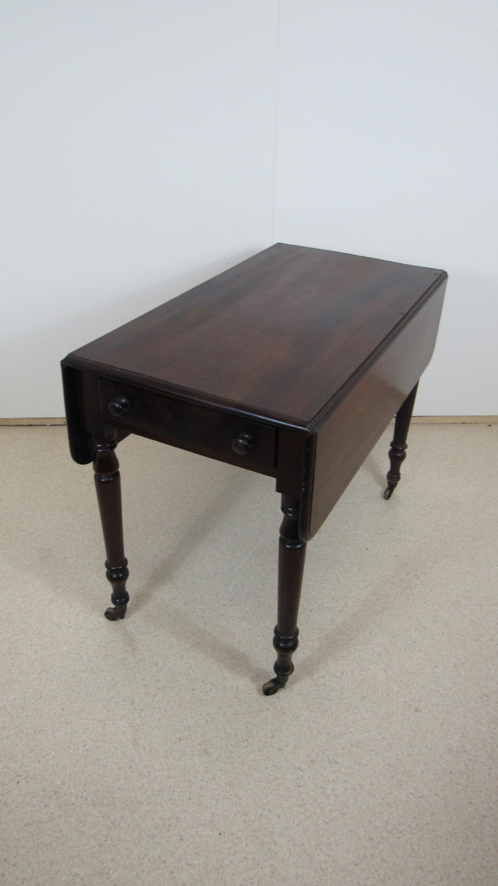 A dark mahogany Pembroke table with two drop leaves, turned legs on brass castors, and a single end drawer with wooden knobs. View XIV