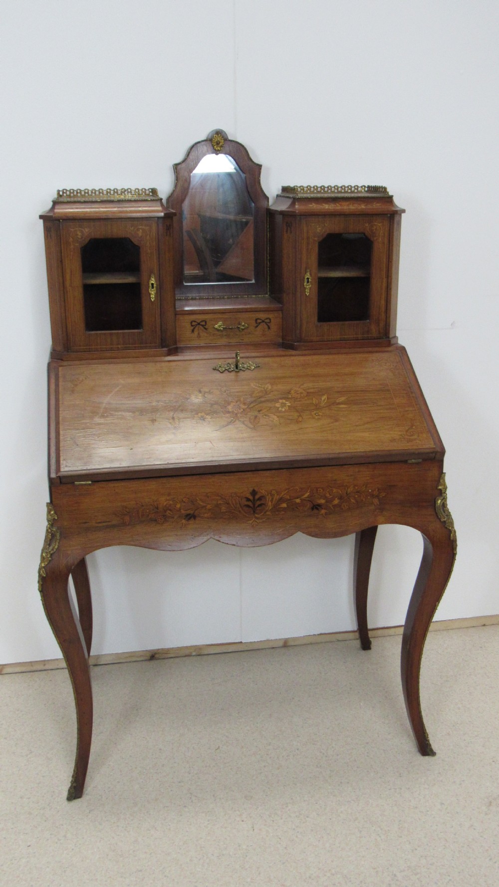 An antique French-style walnut writing bureau with floral marquetry, cabriole legs, brass mounts, and a upper cabinet section featuring small glazed doors and a central mirror. View VI