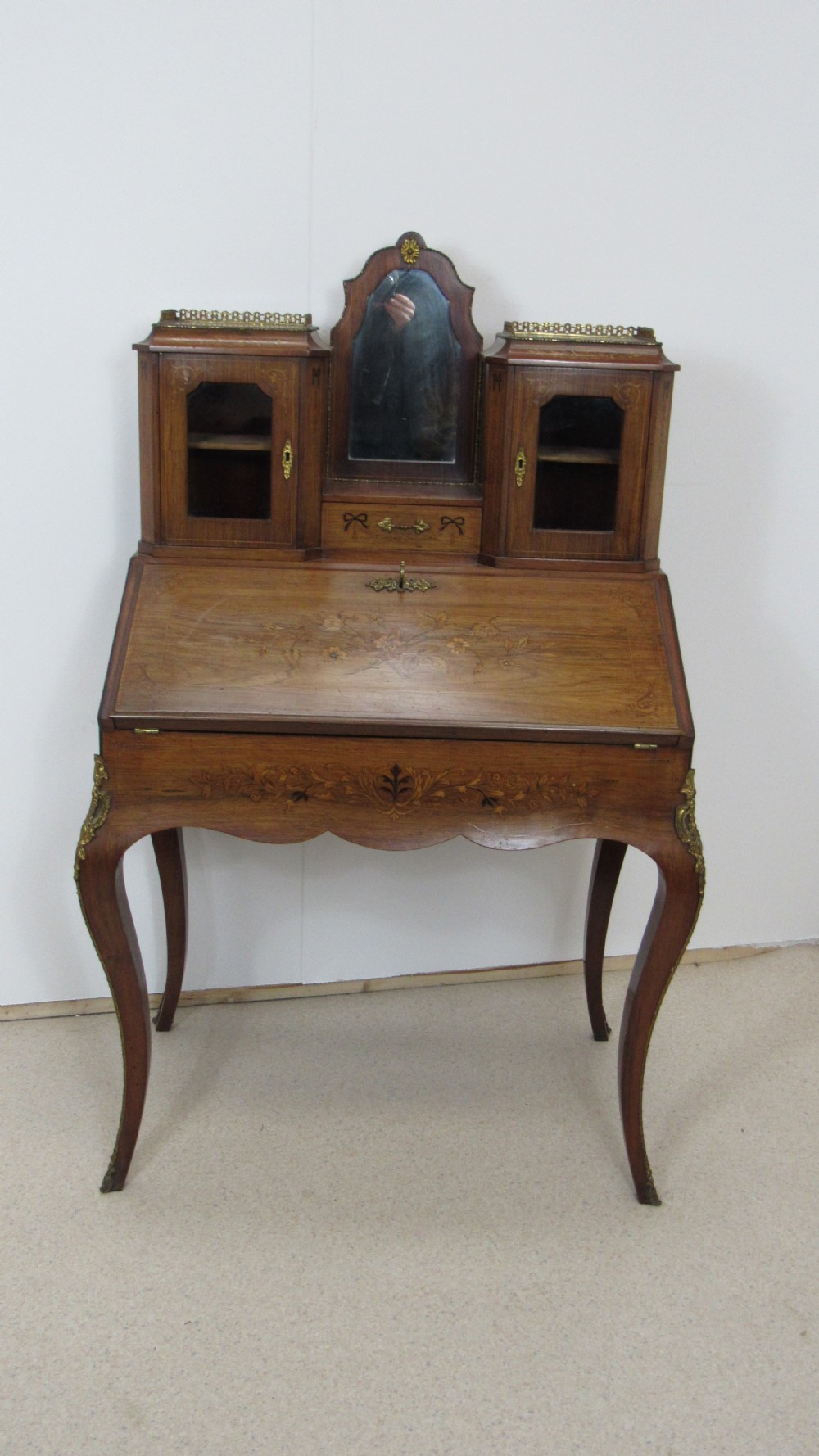An antique French-style walnut writing bureau with floral marquetry, cabriole legs, brass mounts, and a upper cabinet section featuring small glazed doors and a central mirror. View XIII
