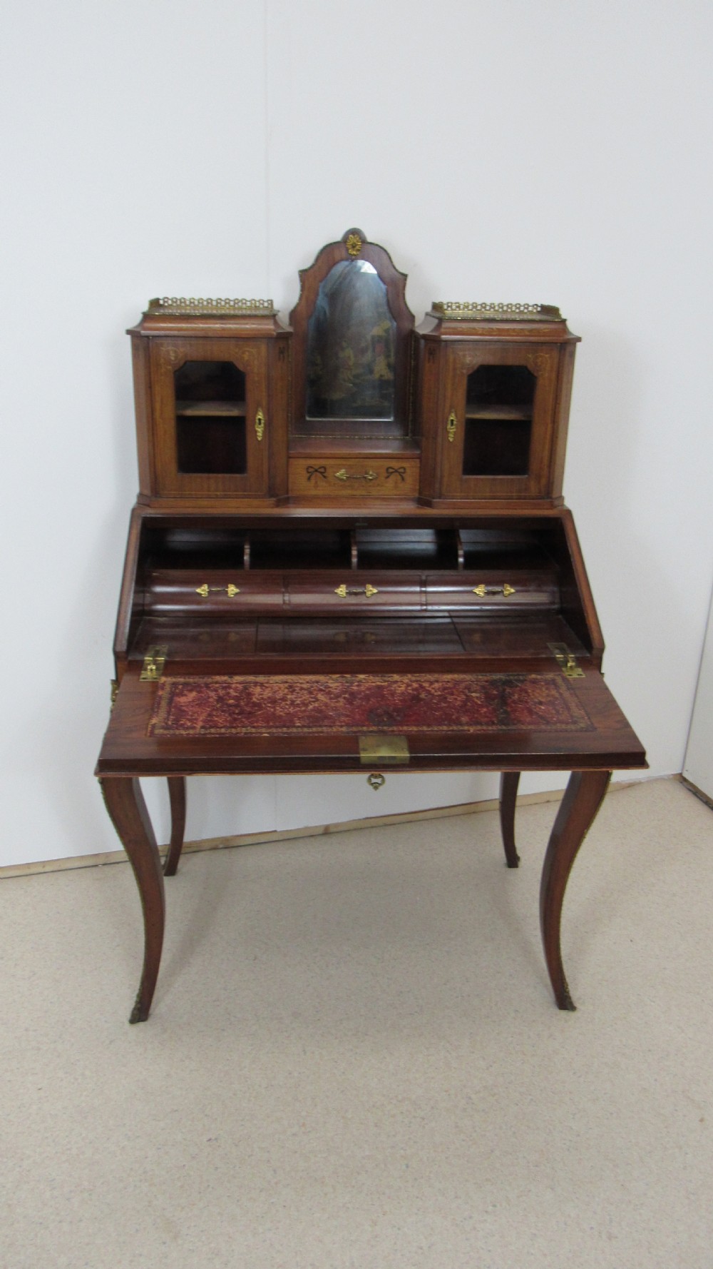 An antique French-style walnut writing bureau with floral marquetry, cabriole legs, brass mounts, and a upper cabinet section featuring small glazed doors and a central mirror. View XIV