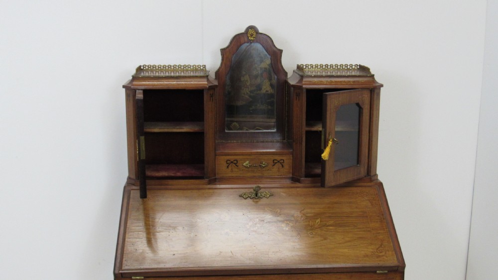An antique French-style walnut writing bureau with floral marquetry, cabriole legs, brass mounts, and a upper cabinet section featuring small glazed doors and a central mirror. View XVII