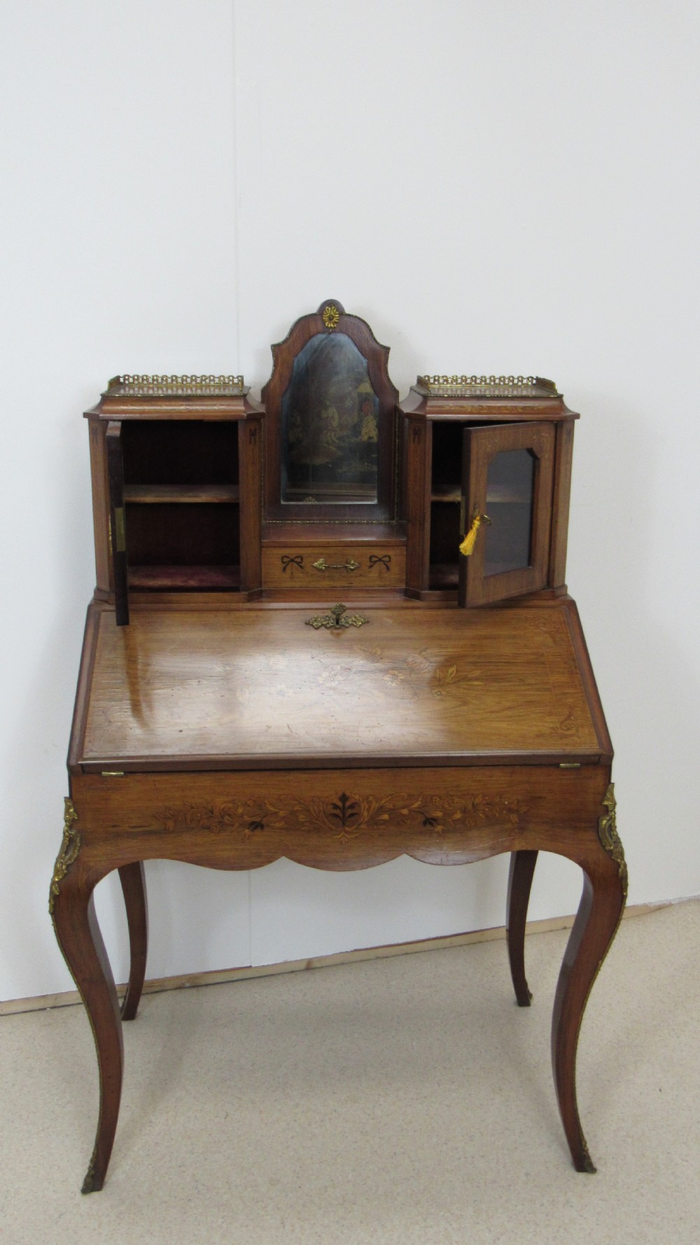 An antique French-style walnut writing bureau with floral marquetry, cabriole legs, brass mounts, and a upper cabinet section featuring small glazed doors and a central mirror. View XVIII